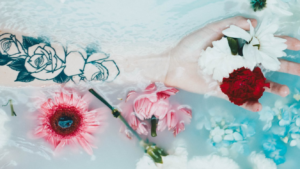 hand in the bath with rose tattoo on arm - pink & red flowers floating in the water