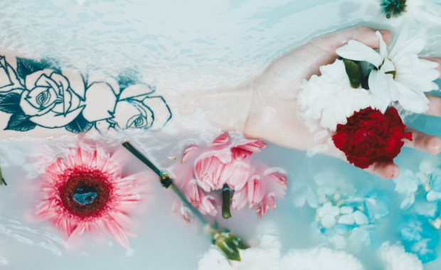 hand in the bath with rose tattoo on arm - pink & red flowers floating in the water